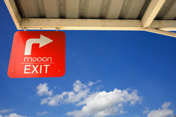 The red background exit sign with white letters under the blue sky and white clouds symbolizes freedom, destination, and place.