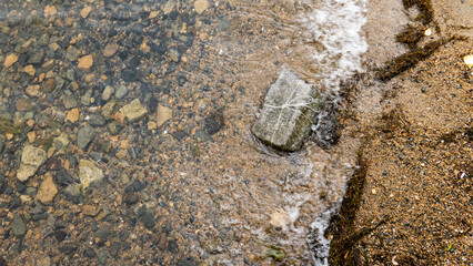 a rectangular stone is tied with a white rope, like a gift. lies on a rocky shore next to the water. waves wash over him. a gift for the summer
