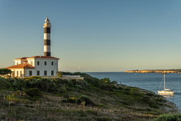 Fototapeta na wymiar General view of the lighthouse of the Majorcan town of Portocolom, at dawn on a sunny day. Maritime navigation image
