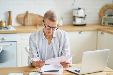 Modern concentrated mature business woman accountant wearing glasses analyzing documents while...