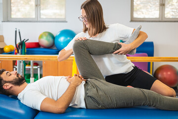 Female physiotherapist doing a treatment for the mobility of the male patient knees and hips.