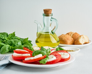 Traditional italian caprese salad. Arranged starter with fresh mozarella, sliced tomatoes, basil leaves, olive oil and baguette. Mediterranean greek food. Delicious healthy antioxidant meal