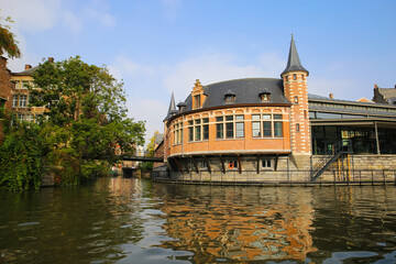 Obraz premium Ghent, Belgium - October 9. 2021: View over river Leie on tourist information center with green tree, bridge against blue morning sky