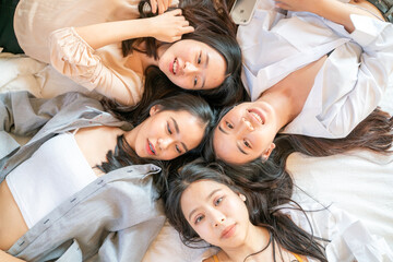 Group of beautiful asian women lying on cozy bed take photo with smartphone
