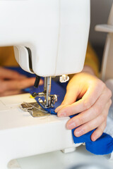 Close up shot of tailor or seamstress sewing or stitching blue navy fabric with professional...