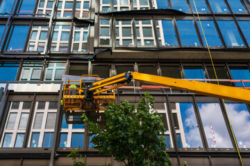 Construction worker using a cherry picker to assemble a facade of a contemporary office building. 