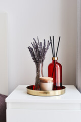 Metal tray with dried lavender, aroma candle and room fragrance duffuser on a bedside table. Home...