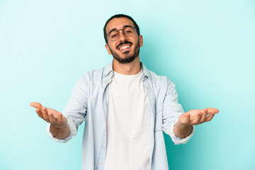 Young caucasian man isolated on blue background showing a welcome expression.