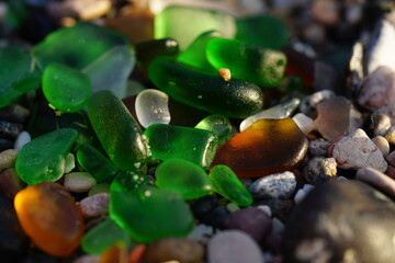 Green and brown glass polished by the sea at a stone beach.