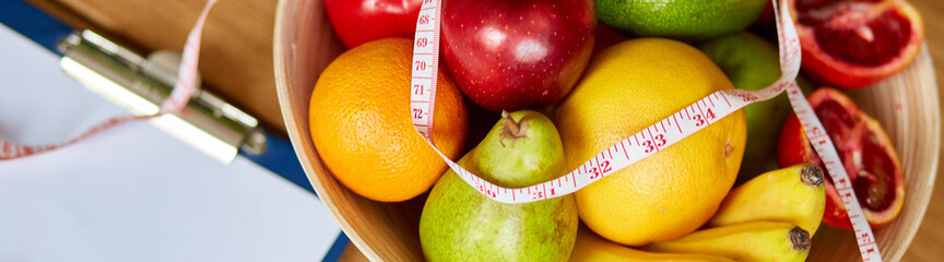 Top view of Nutritionist, dietitian workplace with measuring tape and bowl with healthy vegetables and fruits