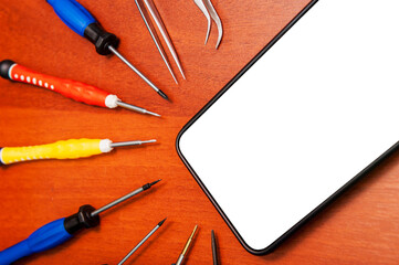 A mobile phone with an empty screen is lying on a table with repair tools, close-up, white screen.