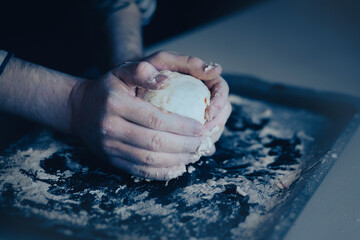 A male chef kneads dough with his hands on a baking sheet with flour to make delicious pastries....