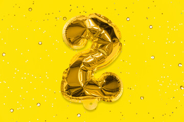 The number of the balloon made of golden foil, the number two on a yellow background with sequins. Birthday greeting card with inscription 2. Top view. Numerical digit, Celebration event, template.
