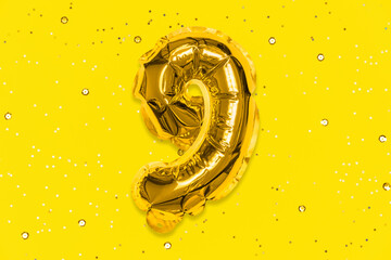 The number of the balloon made of golden foil, the number nine on a yellow background with sequins....