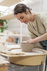 Lady siting on bench with pottery wheel and making clay pot