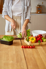 Obraz na płótnie Canvas Woman is preparing vegetable salad in the kitchen, cutting leaf of salad