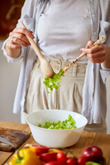 Woman mixing leaf of salad and vegetables ina white bowl