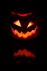 Naklejka premium Close up view of scary Halloween pumpkin with eyes glowing inside at black background