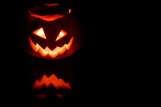 Close up view of scary Halloween pumpkin with eyes glowing inside at black background