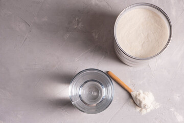 Collagen powder with a glass of water on a gray background with copy space.