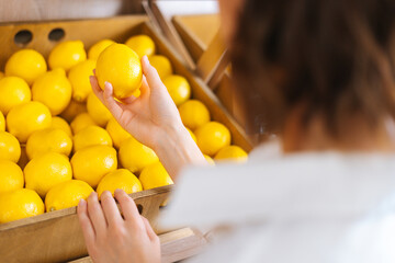 Close-up rear view of unrecognizable young woman choosing lemons at the grocery store picks up...