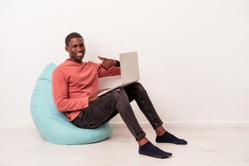 Young African American man sitting on a puff using laptop isolated on white background person pointing by hand to a shirt copy space, proud and confident