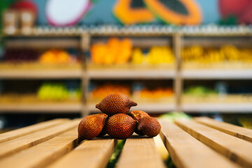 Close-up front view of fresh juicy ripe salak lying on wooden pallet at fruit and vegetables section of grocery store. Tropical exotic fruit selling in supermarket, selective focus, blurred background