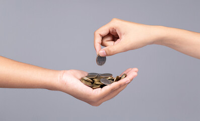 Woman hand putting coin into another hand isolated on gray background.