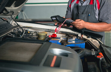 Fototapeta premium Automobile mechanic repairman hands checking car battery with modern tools digital multimeter in car service center.