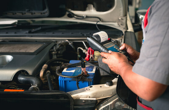 Cropped image of repairman checking car battery using modern tools in service center.