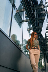 Beautiful girl stands against the background of an office building holding her hands in her pockets. Street photography