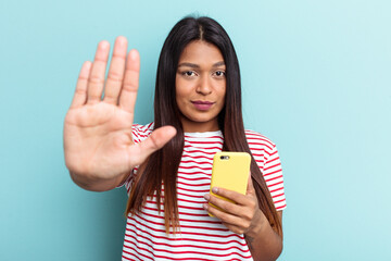 Young Venezuelan woman holding mobile phone isolated on blue background standing with outstretched...