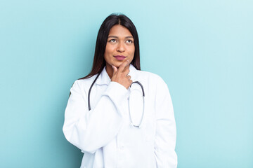 Young doctor Venezuelan woman isolated on blue background looking sideways with doubtful and...