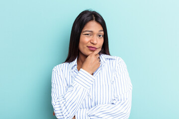 Fototapeta premium Young Venezuelan woman isolated on blue background looking sideways with doubtful and skeptical expression.