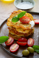 Stack of potatoes fritters served with cherry tomato and olive on plate
