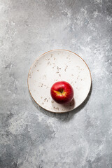 One Red apple on plate on gray concrete surface