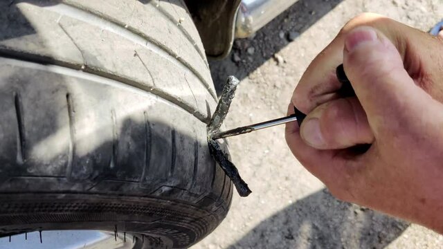 Male hands fixing a puncture of a wheel on the road using an adhesive. Broken wheel on the road. Tire puncture repair tool.