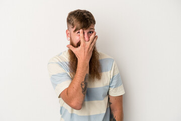 Young caucasian ginger man with long beard isolated on white background blink at the camera through fingers, embarrassed covering face.