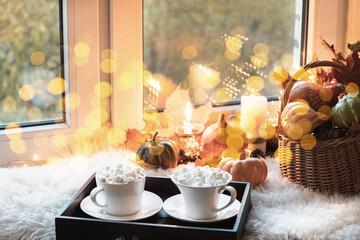 Cozy autumn window sill at home with candles, two coffee, pumpkins, garland and fur. Close up.