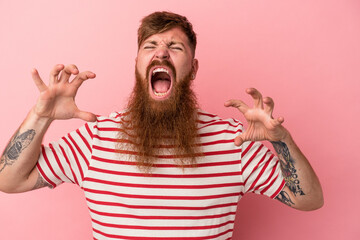 Young caucasian ginger man with long beard isolated on pink background screaming with rage.