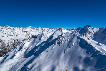 Obraz premium Caucasus Mountains, Panoramic view of the ski slope with the mountains Belalakaya, Sofrudzhu and Sulakhat on the horizon in winter day. Dombai ski resort, Western Caucasus, Karachai-Cherkess, Russia.