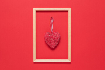 Red heart in a wooden frame on a red textured paper background. Valentine's Day. Top view, flat lay.