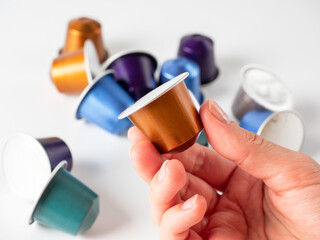 colored aluminum capsule with ground coffee in hand. White background with other capsules lying on it. Modern methods of making coffee. Capsule for coffee machine