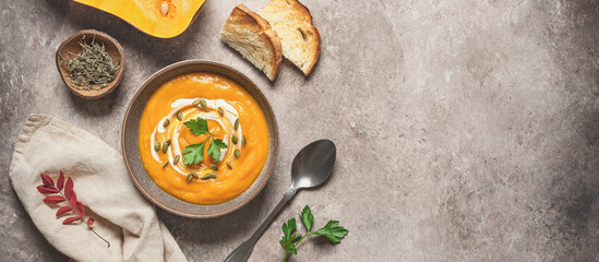 Pumpkin cream soup in a bowl with seeds and toast on a rustic brown background. Warming winter or...