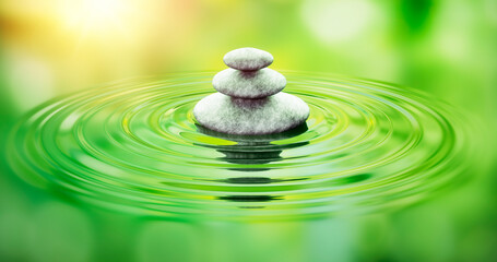 Stack of stones with ripples in the water with green reflections
