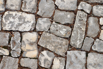 Close-up top view of a cobblestone road. Texture of gray paving stones with ground and dry grass between