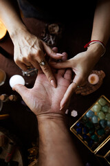 A woman performs a hand reading and draws a line on the person's hand. Top view on her witch altar