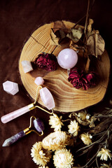 Still life on a wood slice with several rose quartz crystals and dried flowers (egg, rose quartz face roller and several obelisk-shaped stones).Top view
