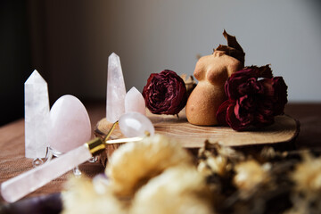 Still life with a clay figure of a pregnant woman decorated with dried roses and various rose quartz crystals (egg, rose quartz face roller) - obrazy, fototapety, plakaty