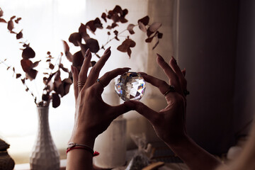 The hands of a woman with long nails and several golden rings hold a crystal ball against the...